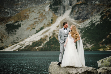 Fototapeta na wymiar The bride and groom near the lake in the mountains. A couple together against the backdrop of a mountain landscape. Morskie Oko (Sea Eye) Lake. Tatra mountains in Poland.