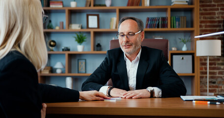 Attractive contented corrupt bearded businessman hiding into drawer a bribe from unfair blonde...