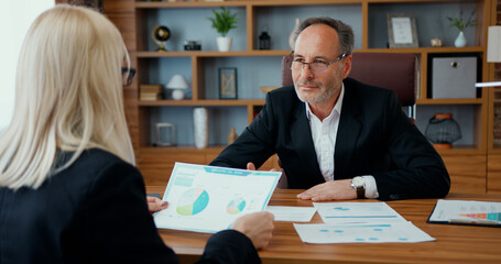 Business concept where handsome satisfied bearded businessman talking with successful blonde female partner,brainstorming on details of joint contract during consultation in good designed workplace