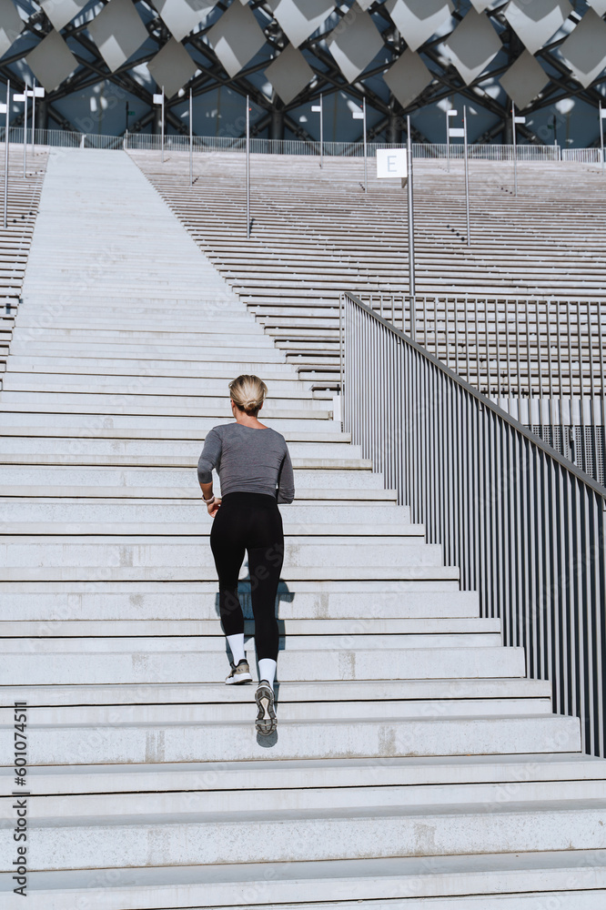 Wall mural Woman athlete wearing female sportswear running and  exercising on staircase between bleachers of outdoor stadium