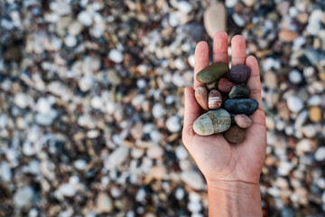 Female hand with heap of pebbles on shingle beach