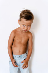 Cute little boy wearing blue jeans posing against white background with silly facial expression