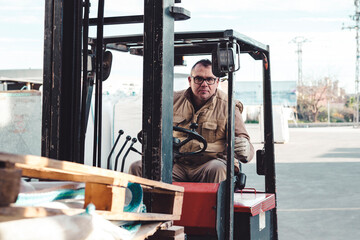 Real worker driving a forklift looking at the camera with a confident attitude