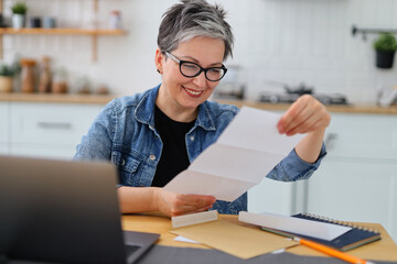Cheerful smiling mature woman looking through mail, invitation to event.