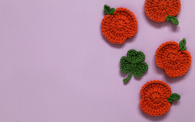 Crochet orange pumpkins and green clover on a violet background. Copy space.