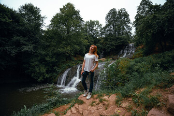 Obraz premium View of young woman standing in front of Dzhurynskyy waterfall. Female tourist, tourism and vacation, active lifestyle. Chervonogorodsky. Nyrkiv Ternopil Oblast Ukraine
