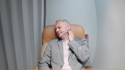 Middle aged caucasian businessman having neck pain while sleeping on seat of private jet. Painful feeling in the neck