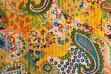 Selective focus closeup photography of pretty colourful cotton bedspread with flowers and paisley patterns and hand embroidery