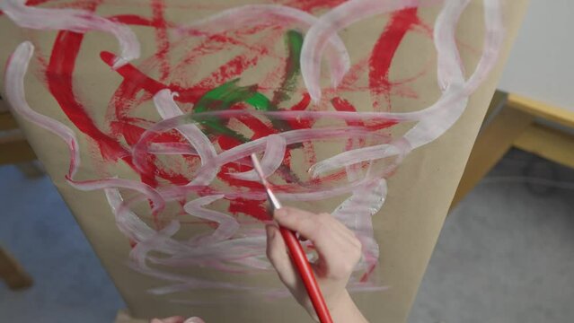 Focused artist works on her masterful creation, using a brush and bright colors. Camera shoots from top to bottom. The young talented artist is focused on her masterful creation, embodying her ideas.