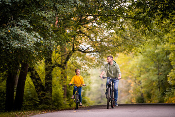 Happy father and daughter ride bicycles in autumn park on sunny day.