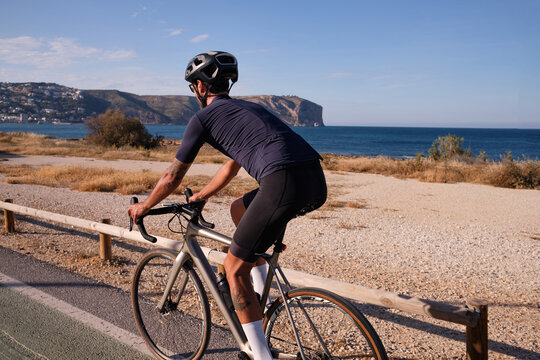 Professional male cyclist riding on bicycle near sea. Spanish cycling holiday. Motivational image. Triathlon concept. Xàbia, Alicante, Spain