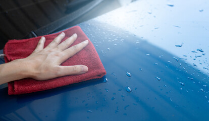 Car wash service. Man hand holding red microfiber cloth polish blue car and water drop after...