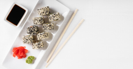 Sushi roll California with salmon, sesame seeds, avocado, cream cheese on white background. Rolls served on white dish with wasabi, ginger and soy sauce. Japanese cuisine food. Top view, copy space