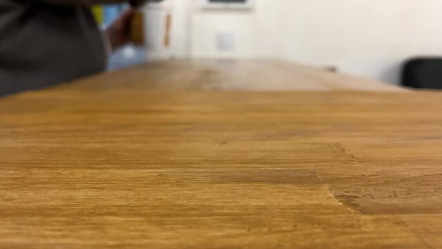 A worker covers a wooden tabletop with transparent varnish in an equipped place. Blurred background