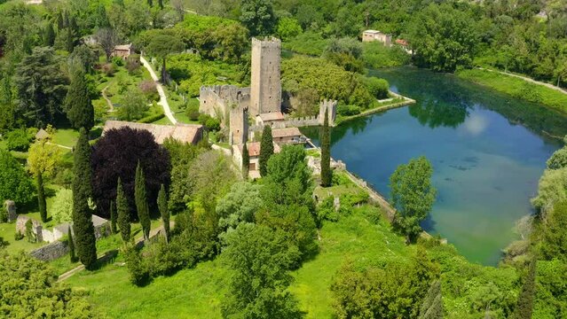 Aerial view of the ruins of the castle and tower located in the Garden of Ninfa, near Latina, Italy. The park is an Italian natural monument and contains a lake and a river. It is empty.