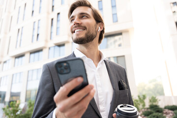 Confident young businessman using cell phone and drinking coffee in the city.