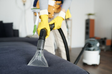 Close-up of worker in protective suit disinfecting sofa with vacuum cleaner