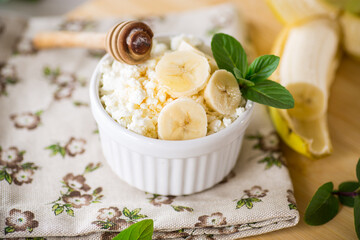 crumbly organic cottage cheese with honey and bananas in a ceramic bowl