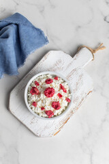 Fototapeta na wymiar Fresh cottage cheese with raspberries in a bowl on a white background