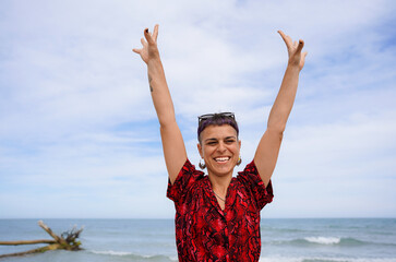 hipster non binary woman in a red leopard shirt on the beach looking at camera. Summer Vacation