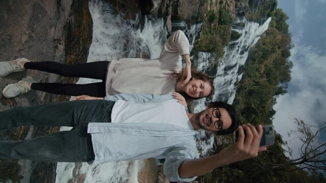 A couple taking selfies at a majestic waterfall in northern Thailand. Slow motion vertical shot