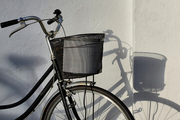 A classic black vintage bicycle, exuding nostalgia and elegance, is parked against the wall, casting a shadow.