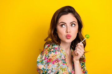 Photo of dreamy shiny lady wear retro flower print blouse licking lollipop looking empty space isolated yellow color background