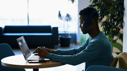 Concentrated young african man in headphones with laptop computer working