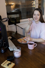 Young beautiful asian girl blogger working at computer at home, eating sandwiches, drinking coffee