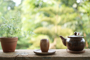 wooden small tea cup and earthenware pot and and plant on wooden table outdoor drinking