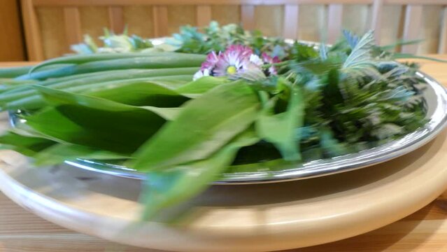 Rotating Plate of healthy freshly picked green leaves of herbs and spices and edible daisy flowers - Allium schoenoprasum, Common nettle, Lovage, Common dandelion, Field balm, Eurasian wild garlic. 