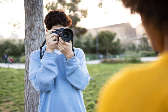 Young man shooting photos near tree on green grass