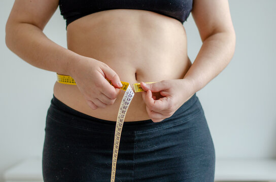 Overweighted woman measuring her belly with a measuring tape