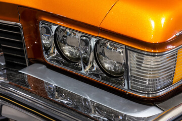 Close-up of the round headlamps of a orange american classic car. Natural patine on the chrome...