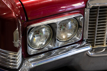 Close-up of the round headlamps of a red american classic car. Natural patine on the chrome details...