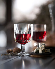 Two glasses of red wine and some cheese on table. Wine in glass goblets, blue cheese diced on small wooden board. Wine tasting. reflective surface. Side view. Blurred background.