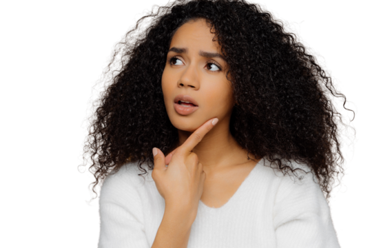 Puzzled woman in white jumper, Afro hair, holds chin thoughtfully. Frustrated expression. Close-up on brown bg