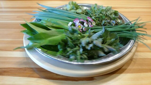 Rotating Plate of healthy freshly picked green leaves of herbs and spices and edible daisy flowers - Allium schoenoprasum, Common nettle, Lovage, Common dandelion, Field balm, Eurasian wild garlic. 