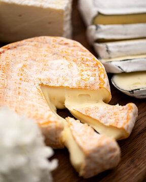 Soft cheese with white mold. Round head of cheese with two cut pieces on table. Cheese with charcoal crust in background. Types of cheese. Camembert. Wooden background. Top view. Soft focus. 