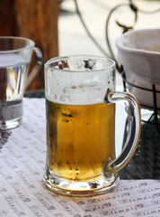 Frosty mug of cold light beer on the table in a restaurant or in a bar. Mug of cold beer, refreshing summer drink. Holiday concept. Live photo of having a glass of beer for lunch in vacation