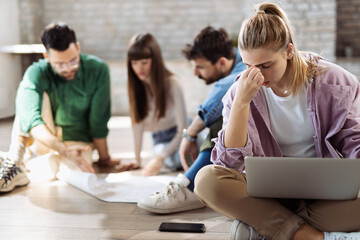 Young businesswoman feeling tired after working on a computer in the office. Her colleagues are in the background