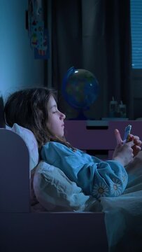 Teen girl scrolling social media texting on smartphone in bed in bedroom at night. Technology, internet, communication and people concept. Dependence on social networks in children. Not healthy sleep.