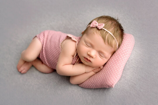 A cute little newborn baby in a pink suit and a pink headband with a butterfly on his head sleeps sweetly. Professional macro photo on a grey background. 