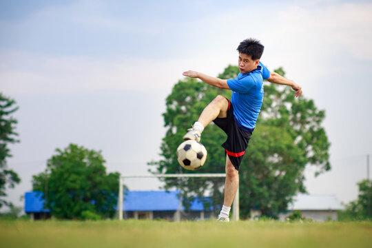 An action sport of soccer football player kicking a ball for exercise in green grass field park. Picture with copy space.