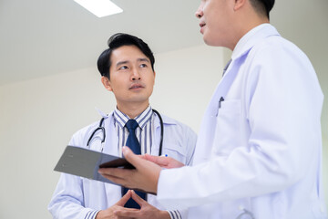 Two Asian doctors discuss a patient's disease, one nervous, the other composed. Illustrates the...