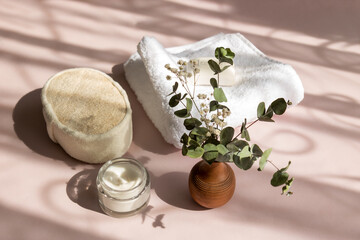 Fototapeta na wymiar set of bath accessories in the sun with shadows, towel, washcloth, cream, soap, a bouquet of green branches in a vase