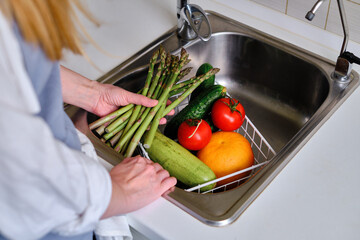 Woman's hands wash vegetables. Fresh farm vegetables on the countertop next to the sink in modern kitchen interior, healthy eating concept