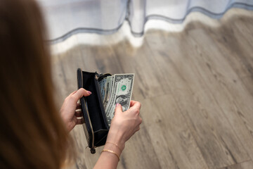 woman counting dollar bills in her wallet, implying the impact of inflation and high prices on her...