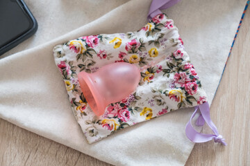 Reusable pink silicone menstrual cup, personal hygiene item, on a cloth bag. view from above
