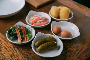 Ingredients for salad with crab in plates on a wooden table.